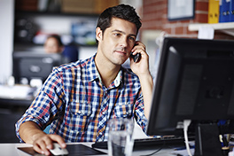 Arbeitsplatz/Büro/junger Mann an Computer/Telefoniert/lächelt in Kamera