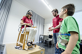 Anlass/Lange Nacht der Forschung/junge Frau mit 3D Brille auf Stuhl/Kontroller in den Händen/Kind und junger Mann schauen zu/Experiment