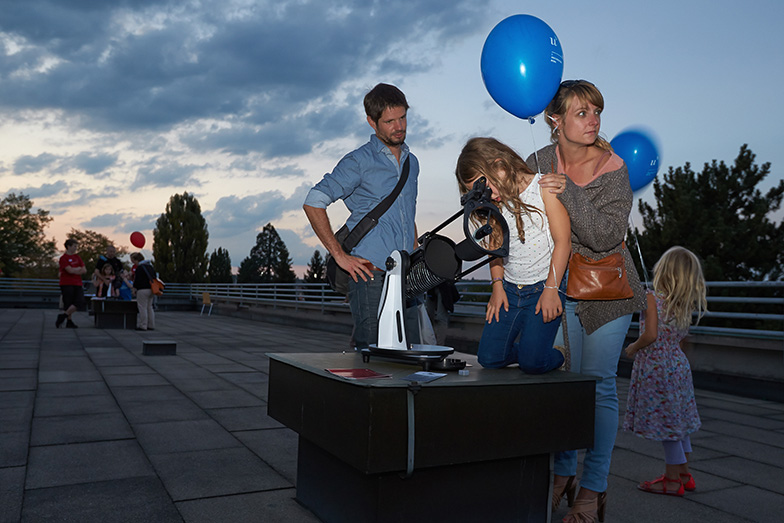 Anlass/Lange Nacht der Forschung/Familie mit blauen Ballonen schaut draussen durch Mikroskop/Nacht